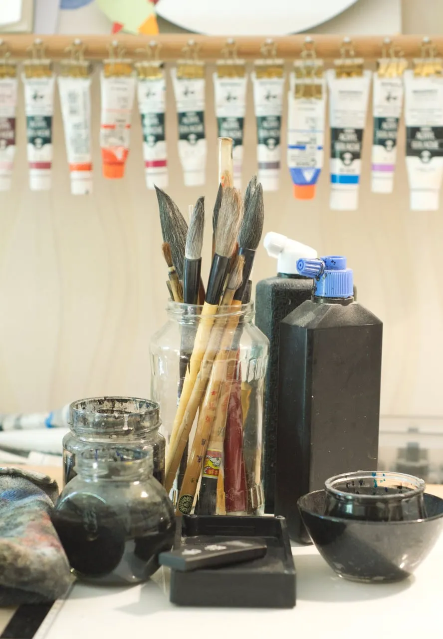 Japanese calligraphy brushes standing beside sumi ink, mixing bowls and other art supplies on Risa’s desk.