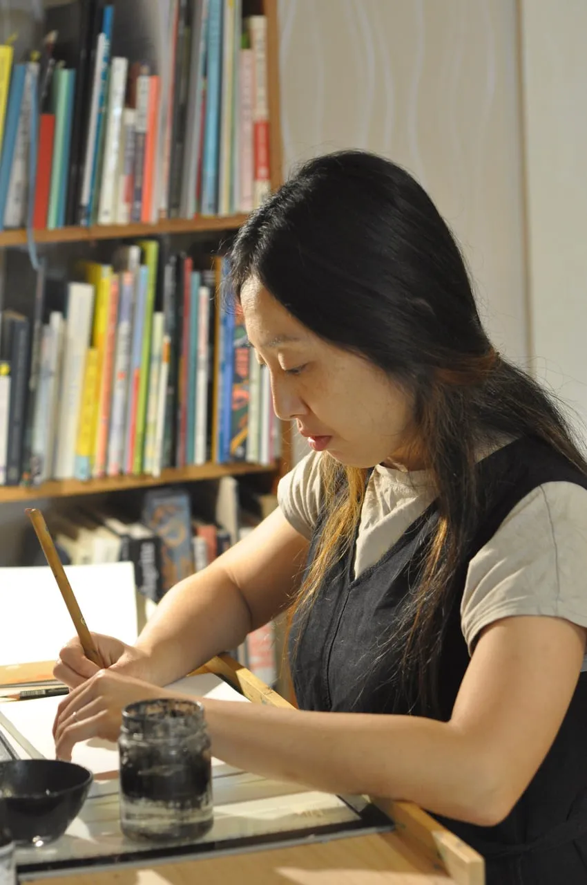 Risa drawing with a Japanese brush and sumi ink at her studio desk.